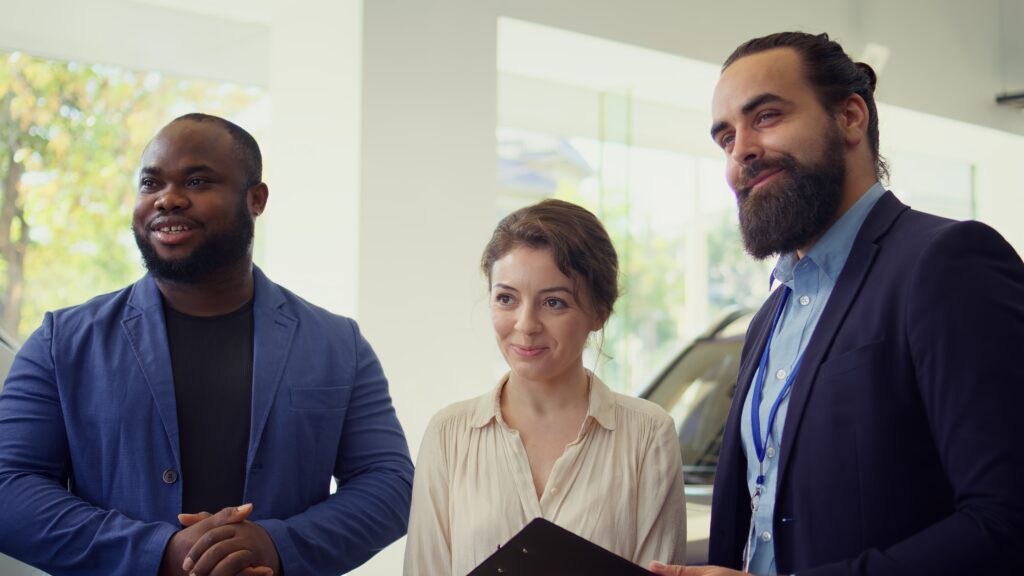 Portrait of happy salesman talking with clients, showcasing dealership vehicle
